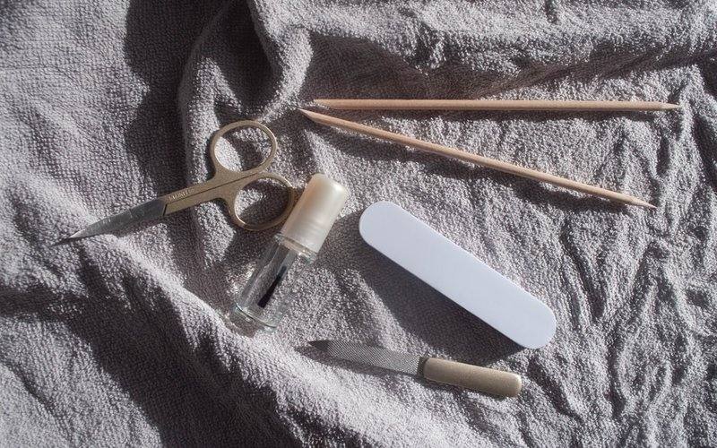 Manicure tools — scissors, cuticle sticks, a nail file and oil — on a grey towel