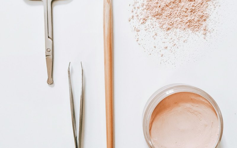 Scissors, tweezers, a brow brush and loose powder laid out on a white surface
