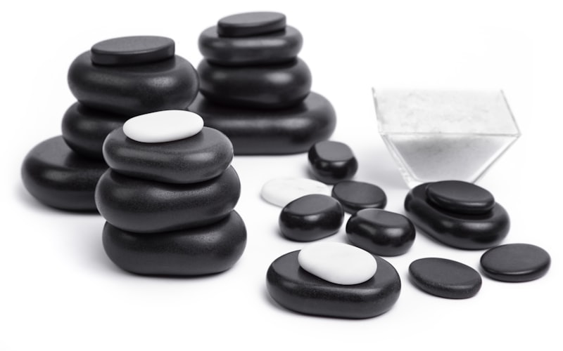 Smooth black basalt massage stones stacked on a white surface