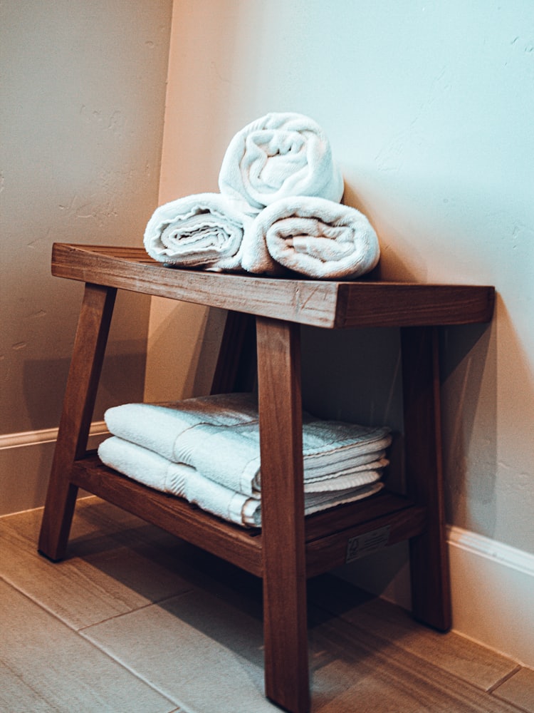 Rolled and folded towels on a wooden bench in a bathroom corner